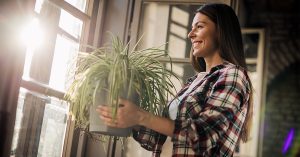 A woman in a plaid shirt holds up a potted houseplant while smiling.