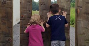 2.	A from-behind view of a female child and a male child, looking through slats in a fence.