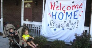 Lizann’s kids in their stroller in front of their “Welcome Home Daddy” sign.