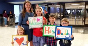 Lizann and her kids holding welcome signs in the airport
