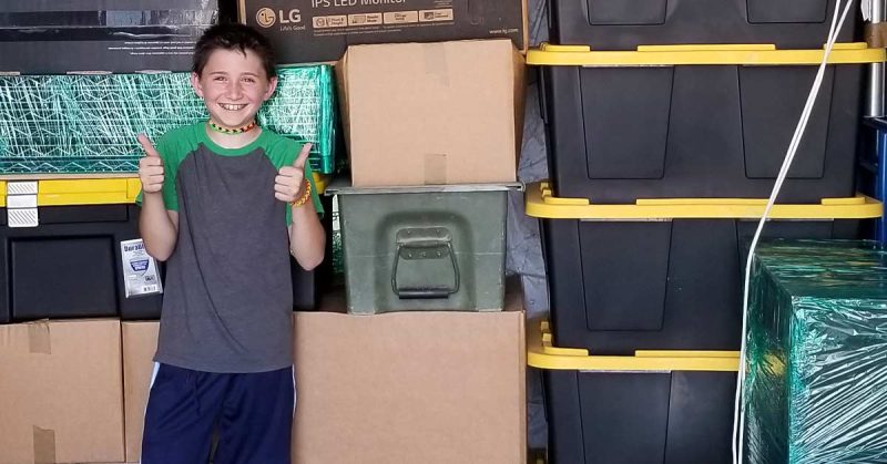 Lizann’s son standing in front of the moving boxes packed away in the moving truck