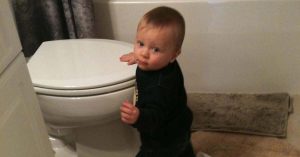 Toddler standing beside a closed toilet in a bathroom, looking over shoulder