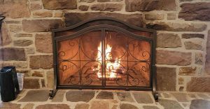 Stone fireplace with wrought iron screen and a lit fire glowing inside