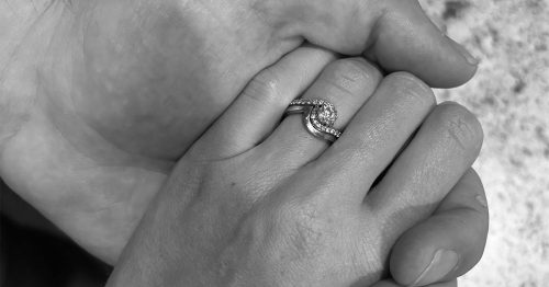 Close-up of two hands gently clasped, one wearing a diamond engagement ring