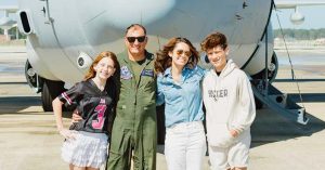 Smiling family poses in front of large military aircraft on sunny runway