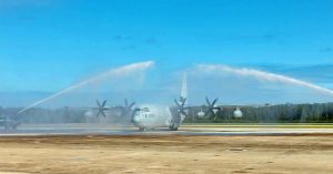 Military aircraft taxis under twin arcs of water in ceremonial return salute on airfield