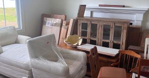 Stacked furniture in a room, including white chairs, a glass-front cabinet and boxed home items