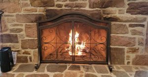 Lit fireplace behind a decorative wrought iron screen, set in a rustic stone hearth