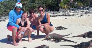 Family poses on a sandy beach with iguanas, enjoying tropical time together.