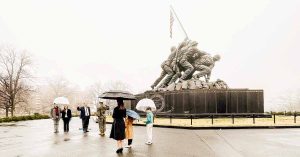 Small group gathers with umbrellas in front of the Marine Corps War Memorial as a military member raises their right hand in oath.