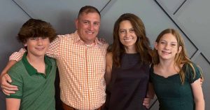 Kristi’s family of four posing together against a gray wall.