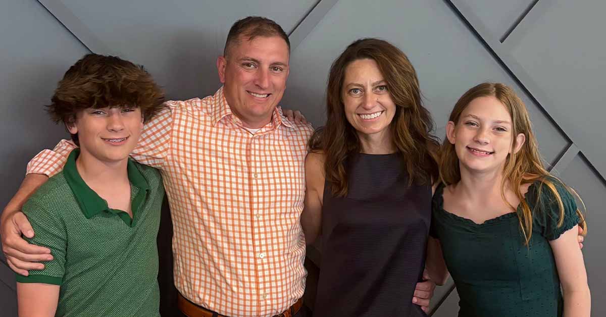 Kristi’s family of four posing together against a gray wall.