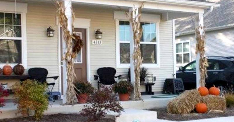 House porch decorated for fall with pumpkins, hay bales, corn stalks, and a wreath on the front door.