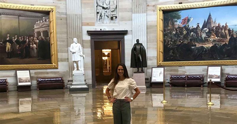 Kristi stands next to historic statues and large framed paintings on the walls behind her.