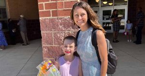 Kristi and her daughter smiling outside a building, her daughter holding a colorful bouquet of flowers