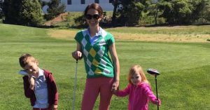 Kristi and her two children stand on a grassy golf course holding golf clubs, smiling outdoors