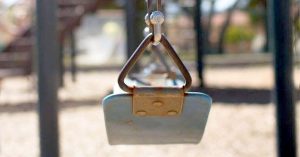 Empty playground swing hanging still with blurred park equipment in the background