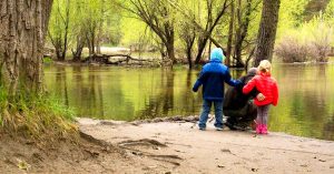 Kristi’s family stands by a calm river in a wooded area with green trees