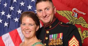 Lizann and her husband smile in front of American and Marine Corps flags, with her husband wearing a decorated military uniform.