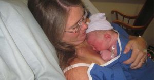 Lizann holds her newborn baby against her chest, both resting in a hospital bed.
