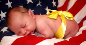 A sleeping newborn lies on an American flag blanket with a yellow ribbon tied around them.