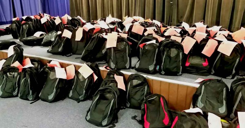 Rows of backpacks with tags attached, organized for distribution.