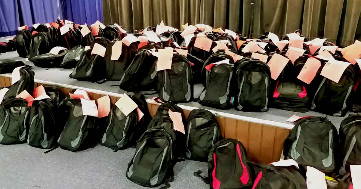 Rows of backpacks with tags attached, organized for distribution.