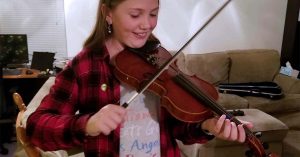 Lizann’s daughter playing a violin in a living room.