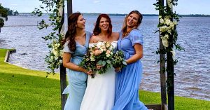 Lauren and bridesmaids posing under a floral arch beside a lake.