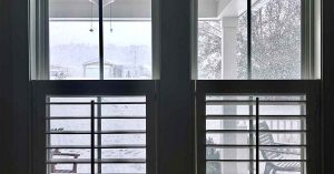 Snow-covered backyard viewed through large windows during a winter storm.