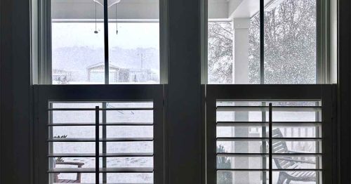 Snow-covered backyard viewed through large windows during a winter storm.