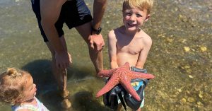 Sydney’s child holding a large starfish while standing in shallow water.