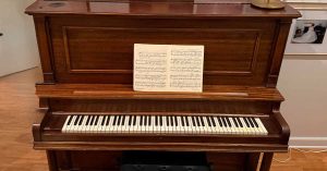 A piano with open sheet music sits against a wall, decorated with framed photos and artwork.