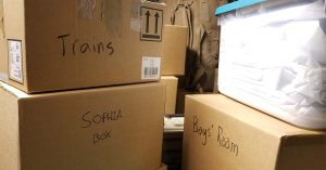 Stacked moving boxes labeled “Trains,” “Sophia box,” and “Boy’s Room” fill a space, showing organized packing during a move.