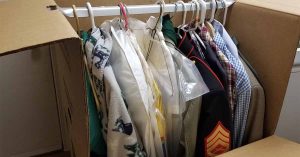 Clothes on hangers are neatly packed inside an open moving box.