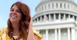 Lauren smiling in a yellow patterned top in front of the U.S. Capitol building with the dome blurred in the background.