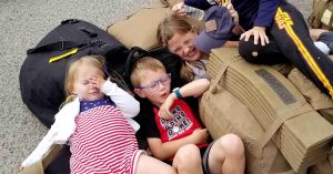Lizann’s children laughing and resting, with one child covering their eyes and another holding a water bottle.