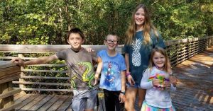 Lizann’s children standing together on a wooden boardwalk surrounded by trees, smiling during a nature walk.