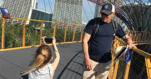 Kristi’s family exploring an elevated outdoor walkway in a city, as a child takes a photo of Kristi’s husband leaning on the railing.