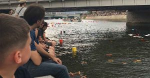 People river watching floating lanterns drift beneath a bridge during an outdoor evening event.