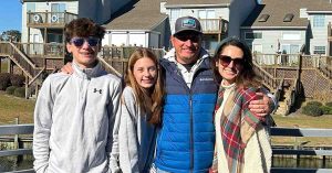 Kristi and her family smiling together outdoors in front of waterfront homes.