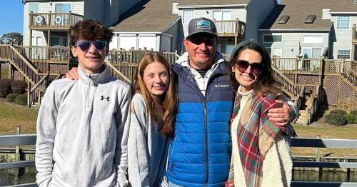 Kristi and her family smiling together outdoors in front of waterfront homes.