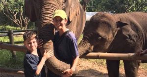 Kristi and her son smiling while interacting with elephants at a wildlife park.