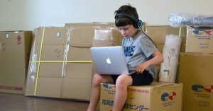A child on a laptop sitting on top of a moving box