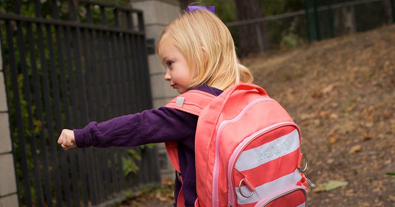 A young girl wearing a pink backpack making a fist