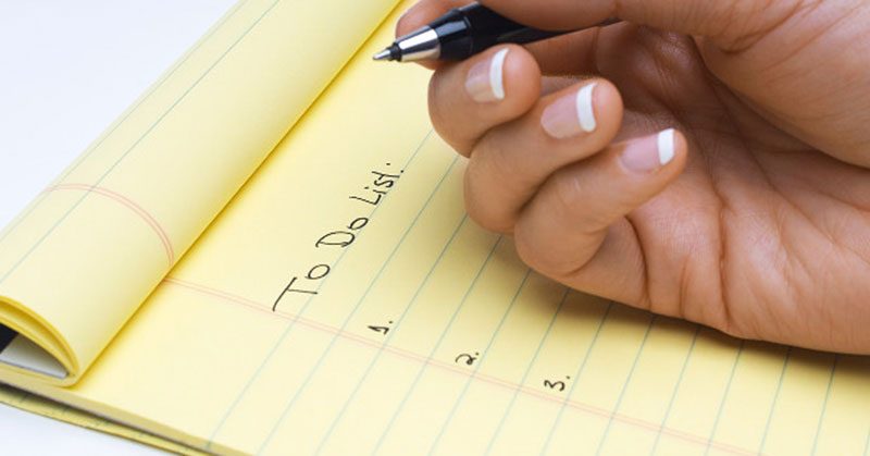 A person writing a to-do list in a yellow notepad