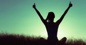 Silhouette of a woman giving two thumbs up in front of a sunrise