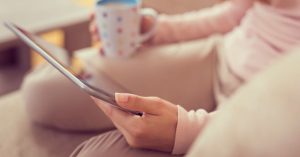 Closeup of a woman holding a tablet and a cup of coffee
