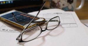 glasses next to phone calculator on top of tax forms