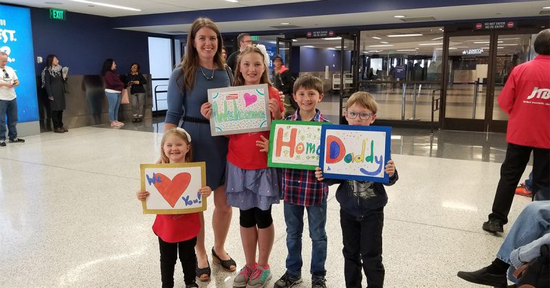 family at the airport holding up welcome home signs for their service member